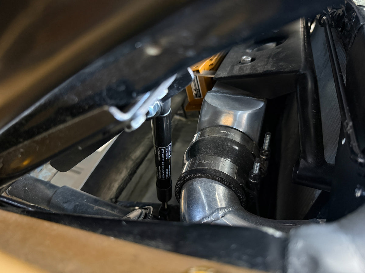 Side detail of a Skillard hood strut installed beside the radiator and intercooler piping on a Datsun 280ZX.