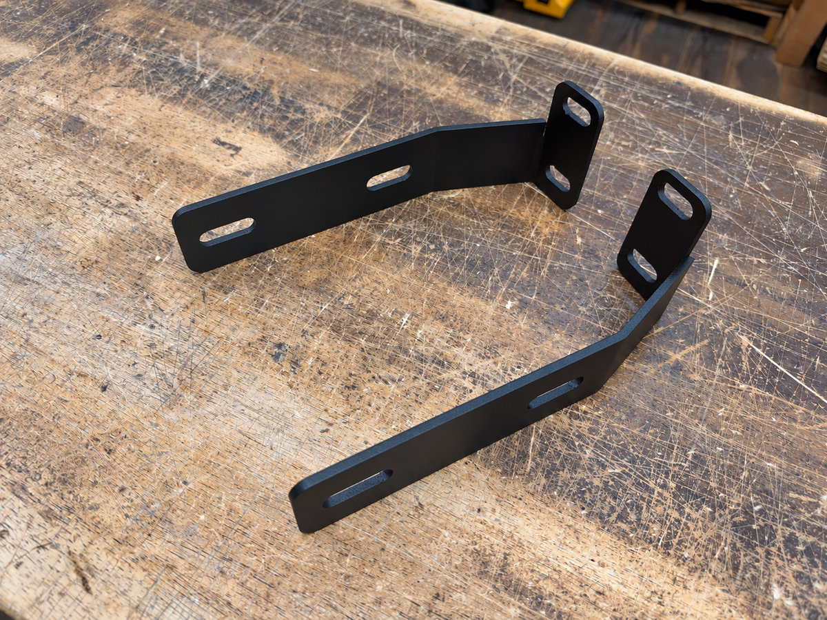 Pair of black Skillard tucked front bumper brackets for a Datsun 280ZX, showing slotted mounting holes and offset bends.