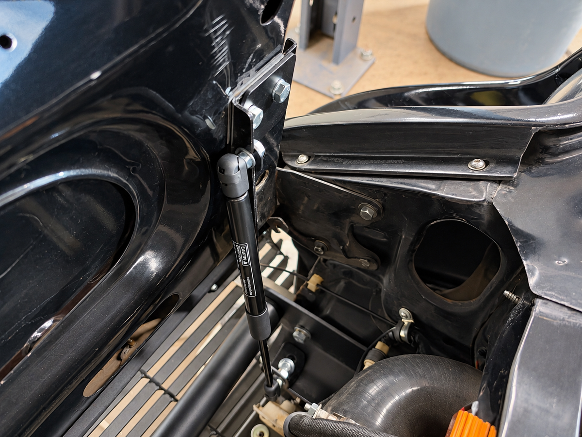 Close view of a Skillard hood strut installed on a Datsun 280ZX between the hood hinge and lower mounting bracket.