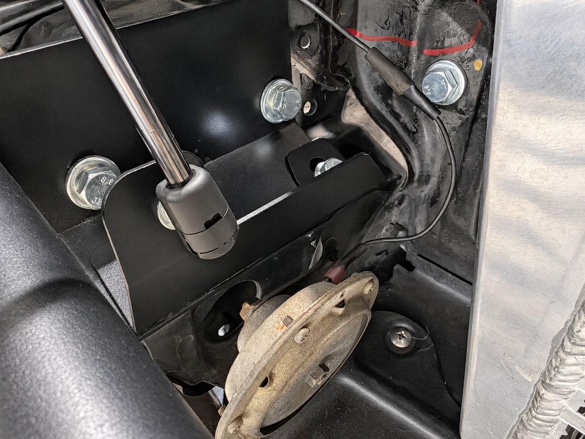 Close view of the black powder-coated steel lower hood strut bracket installed on a Datsun 280ZX.