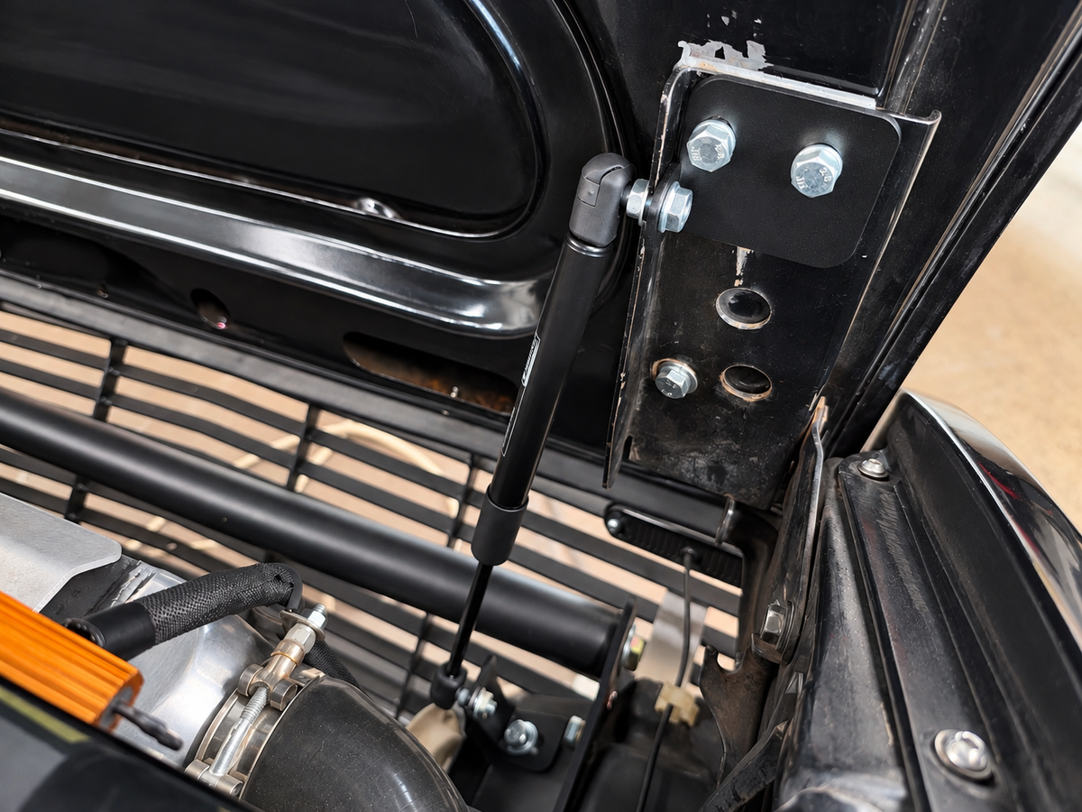 Close view of the black powder-coated aluminum upper hood strut bracket installed on a Datsun 280ZX.